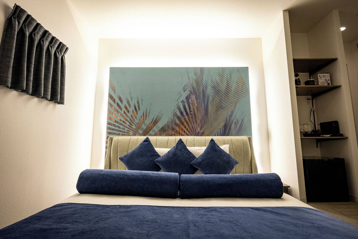 Ein Schlafzimmer mit Bett, Kissen, einem Bild, einem Vorhang und einem Regal mit Gegenständen.
