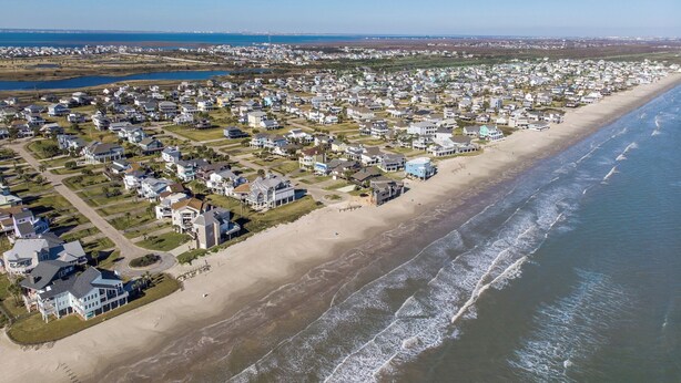 Une zone résidentielle côtière avec des maisons le long de la plage, un ciel dégagé et une vue lointaine sur l’océan.