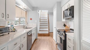 Une cuisine moderne avec des meubles blancs, un escalier en bois et un four à micro-ondes.