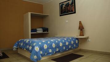 A bedroom with a bed, a wardrobe, a shelf with folded clothes, a lamp, and a painting on the wall.