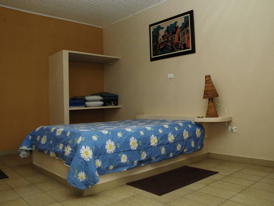A bedroom with a bed, a wardrobe, a shelf with folded clothes, a lamp, and a painting on the wall.