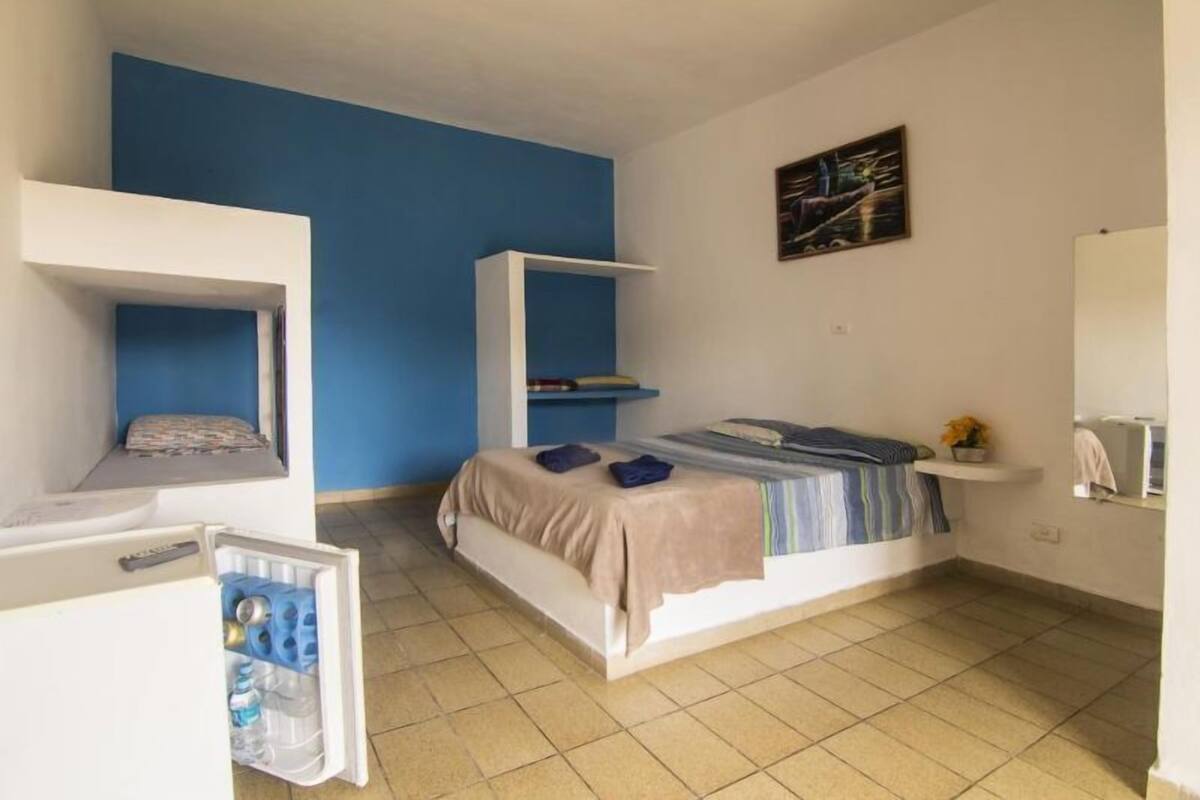 Une chambre à coucher de taille réduite, comprenant un lit, une petite étagère blanche, une armoire blanche et une étagère fixée au mur.