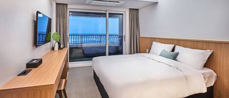 A hotel room with a bed, a desk, a TV, and a balcony with a view of the sea.