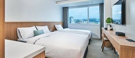 A hotel room with two beds, a desk, a TV, and a view of the city.