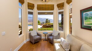 A room with a view of mountains, a sofa, two armchairs, a small table, and plaid curtains.