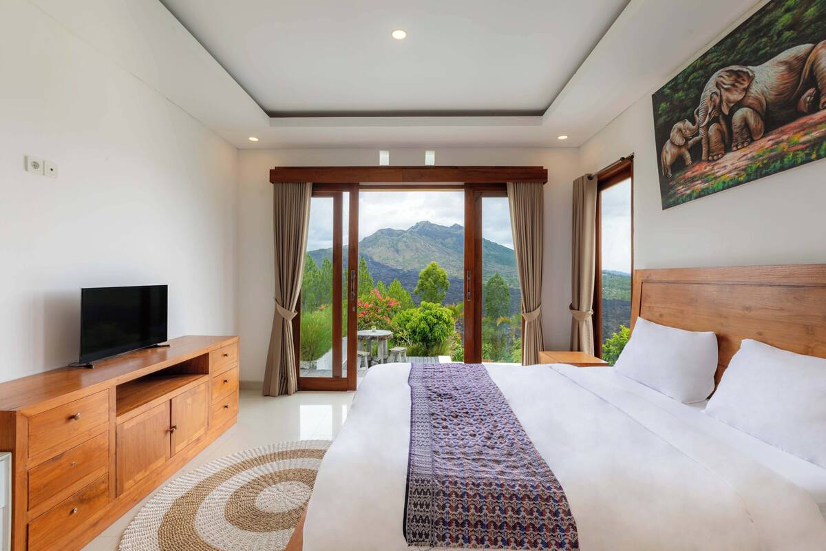 A bedroom with a large bed, a TV on a wooden cabinet, and a painting of elephants on the wall.