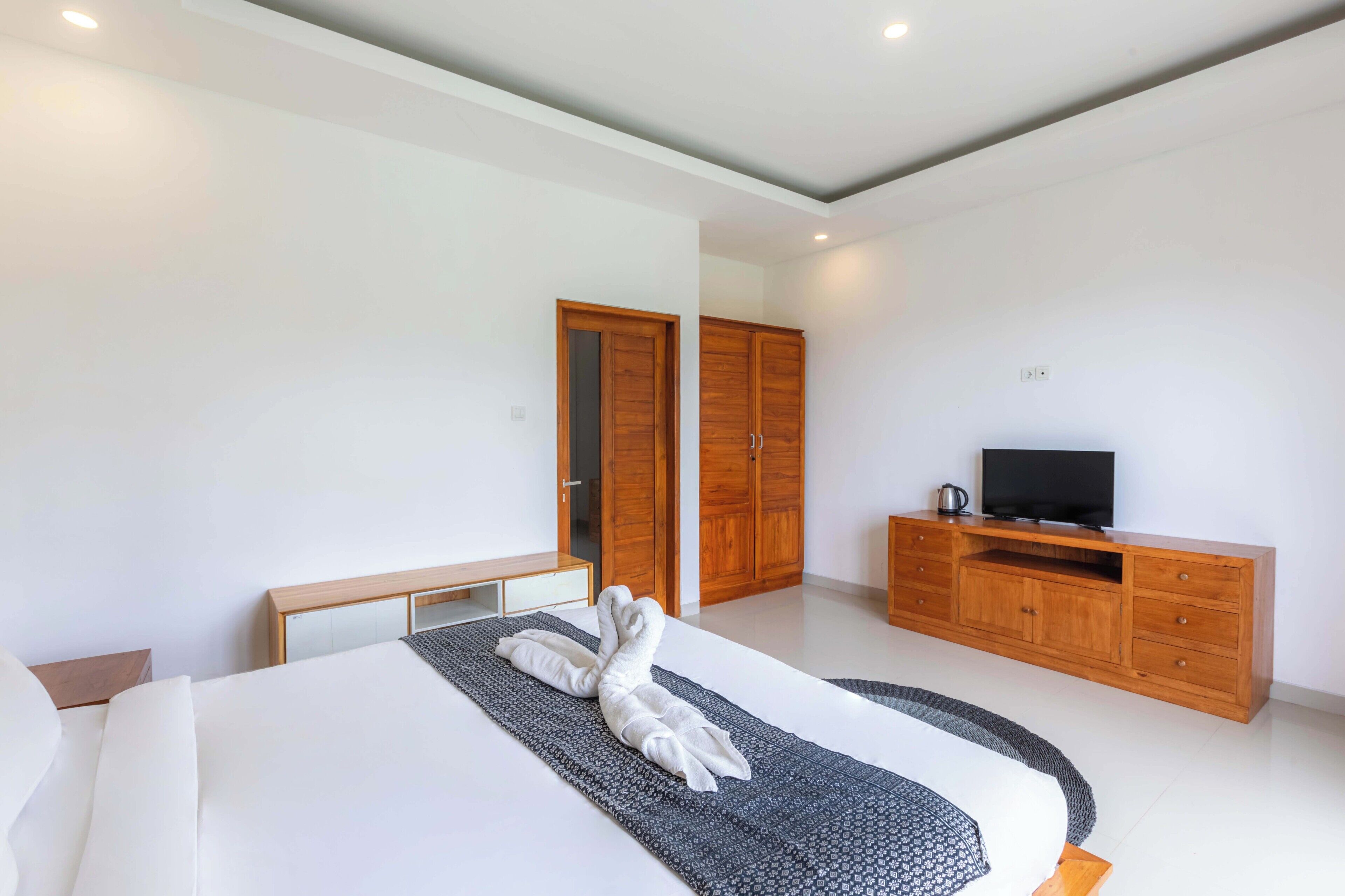 Une chambre d’hôtel moderne avec un grand lit, une armoire en bois et un téléviseur posé sur une commode en bois.