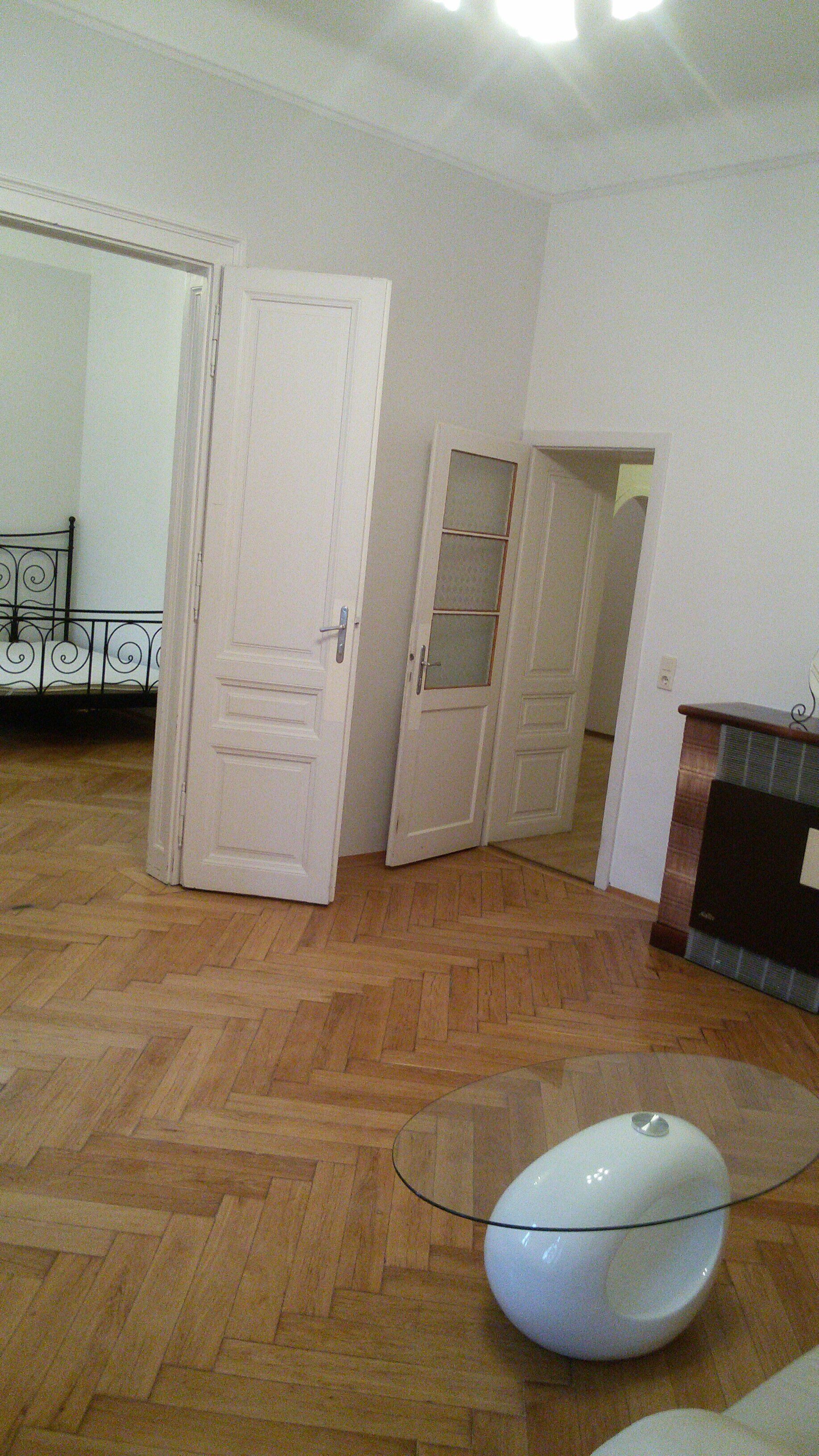 A room with wooden parquet flooring, a glass table, and white doors.