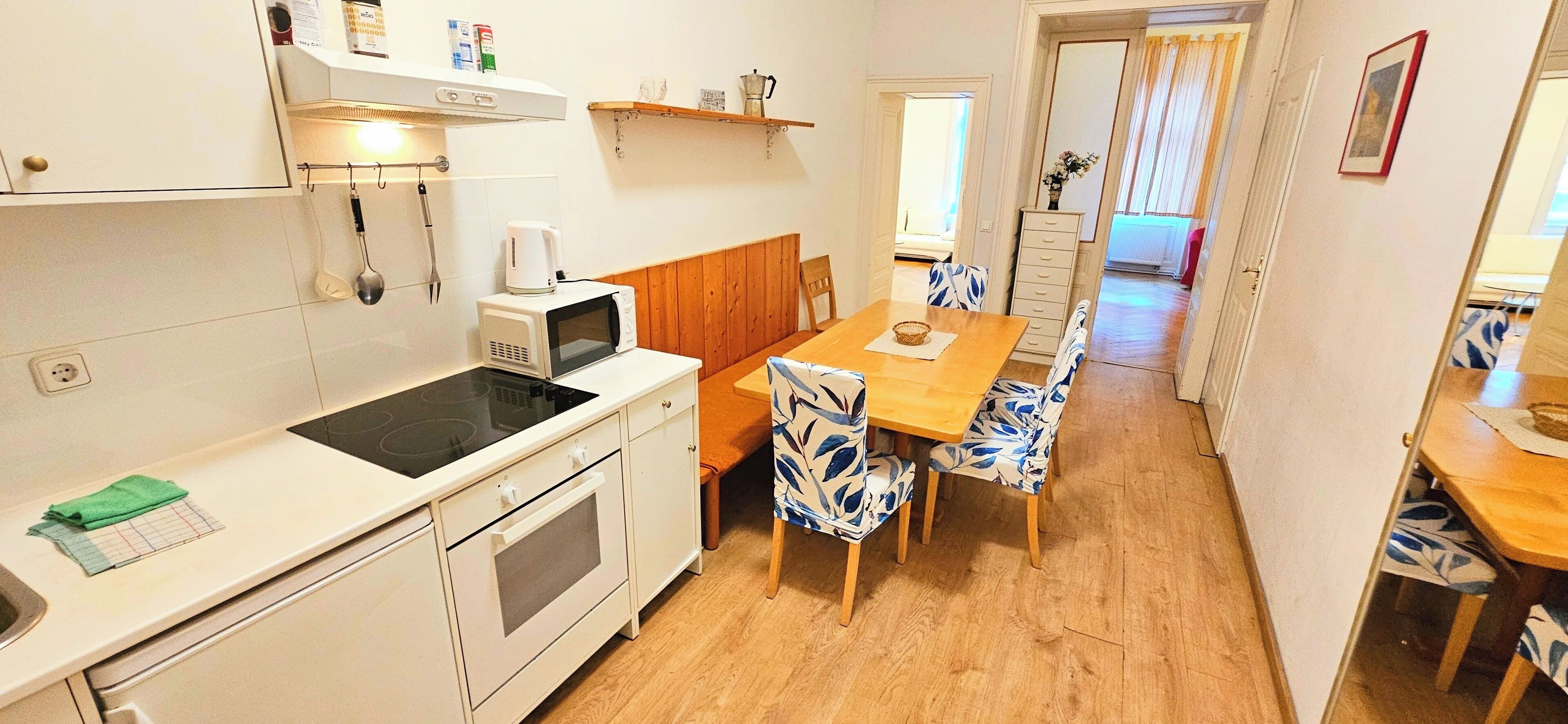 A compact kitchen with a microwave, stove, and wooden dining table with patterned chairs.