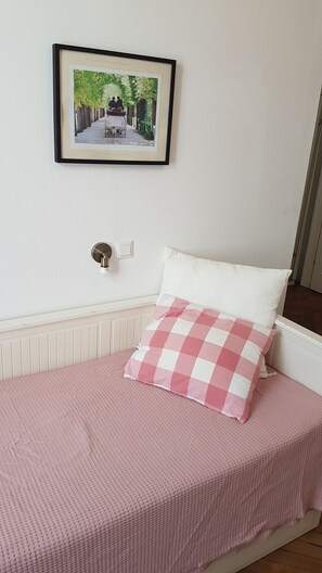 Een slaapkamer met een bed, een geruit kussen, een ingelijst schilderij aan de muur en een lichtschakelaar.