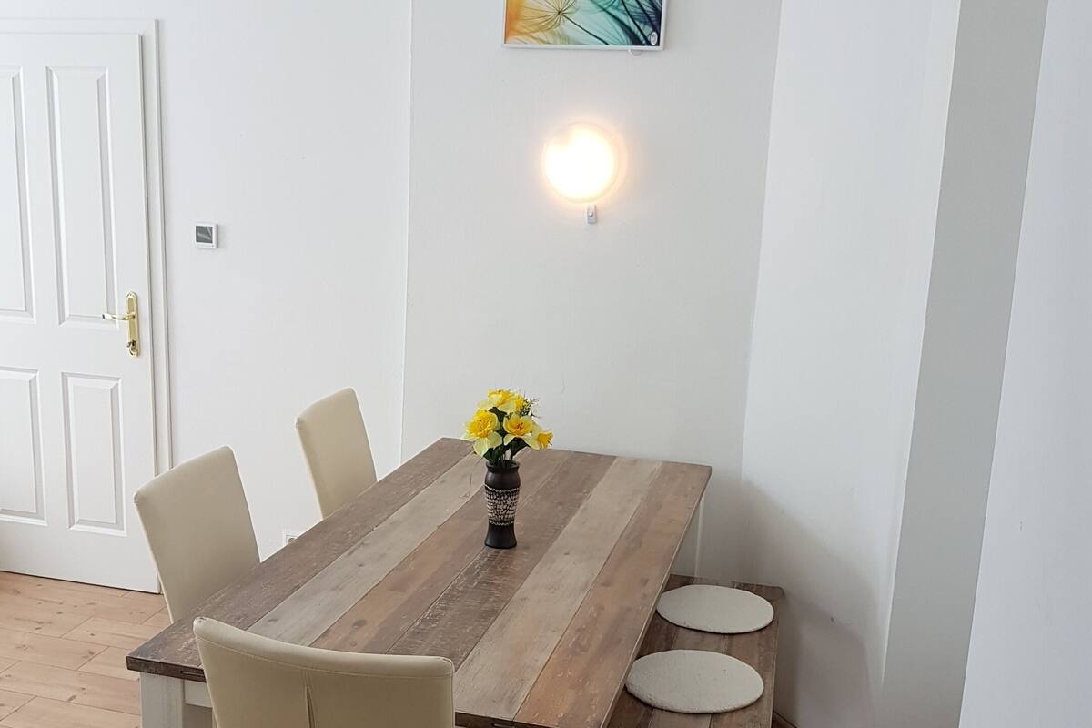 A dining area with a wooden table, four chairs, and a vase with yellow flowers.