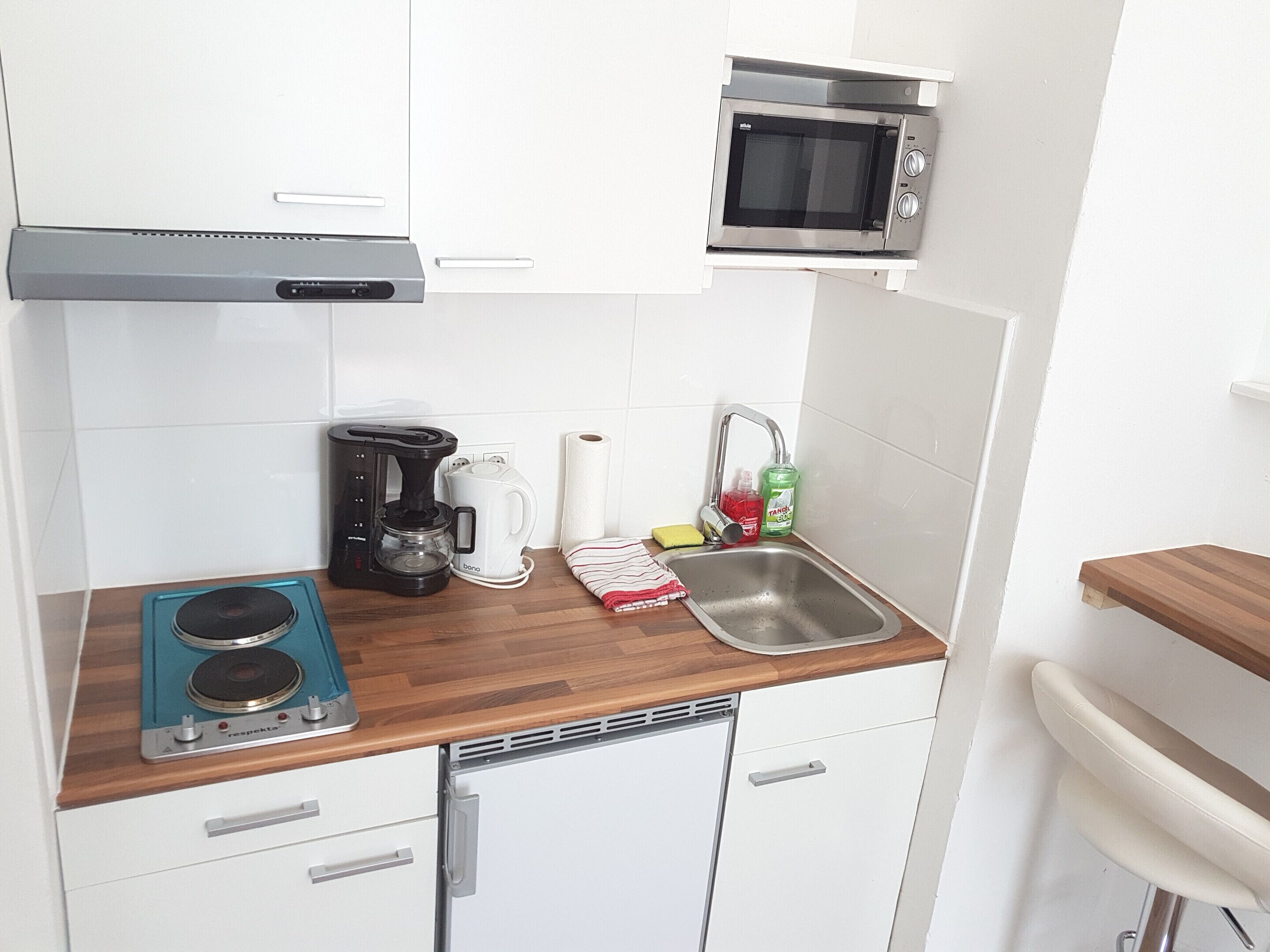 A compact kitchen with a microwave, coffee maker, kettle, and a sink.