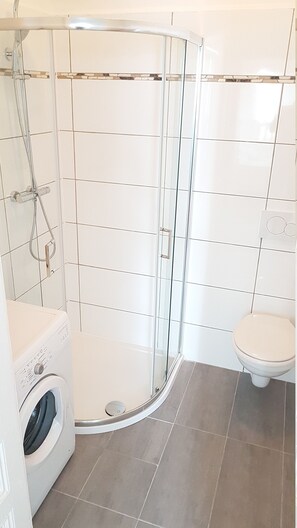 Een moderne badkamer met een glazen douchecabine, toilet en een wasmachine.