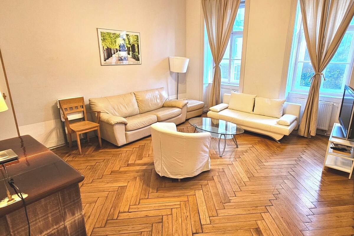 A living room with a herringbone wooden floor, a sofa, a chair, a lamp, and a television.