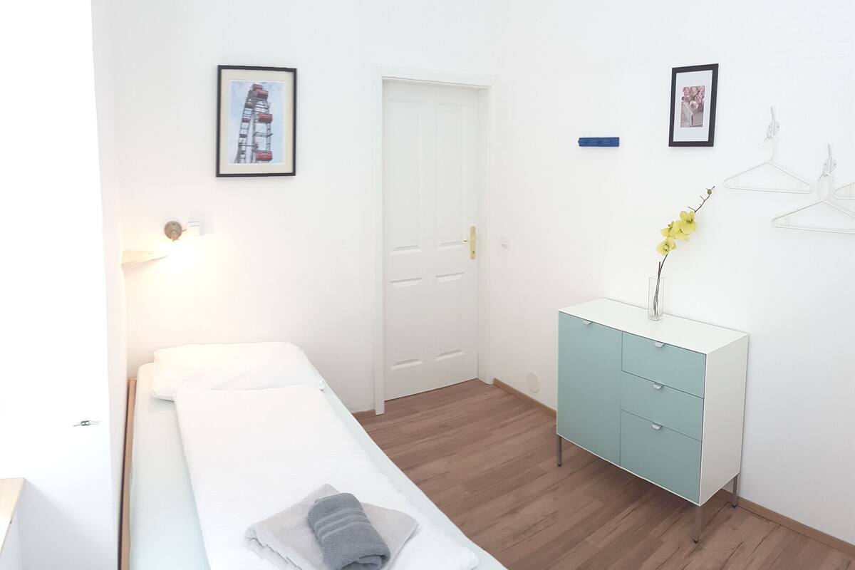 A bedroom with a bed, a wardrobe, a desk, and two framed pictures on the wall.
