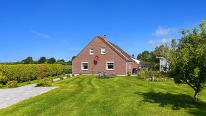 Et rødstenshus med skråt tag, græsplæne med to liggestole og en hæk i forgrunden.