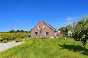 Ein rotes Ziegelhaus mit geneigtem Dach, einer Rasenfläche mit zwei Liegestühlen und einer Hecke im Vordergrund.