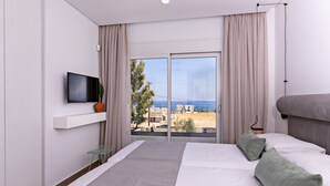 A modern hotel room with a large bed, a flat-screen TV, and a balcony with a view of the sea and buildings. - Constantinos Villa, Sublime Island Εscape.Walking distance to the beach & shops (Panormos in Rethymno)