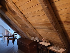 A cozy attic room with wooden beams, a wooden chest, a small table with a vase, and a chair. - Holiday room 1 - RUMPELSTILZ baking and shower barn (Steinhagen)