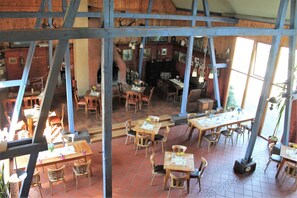 A rustic dining area with wooden tables and chairs, a fireplace, and a view through a wooden structure.