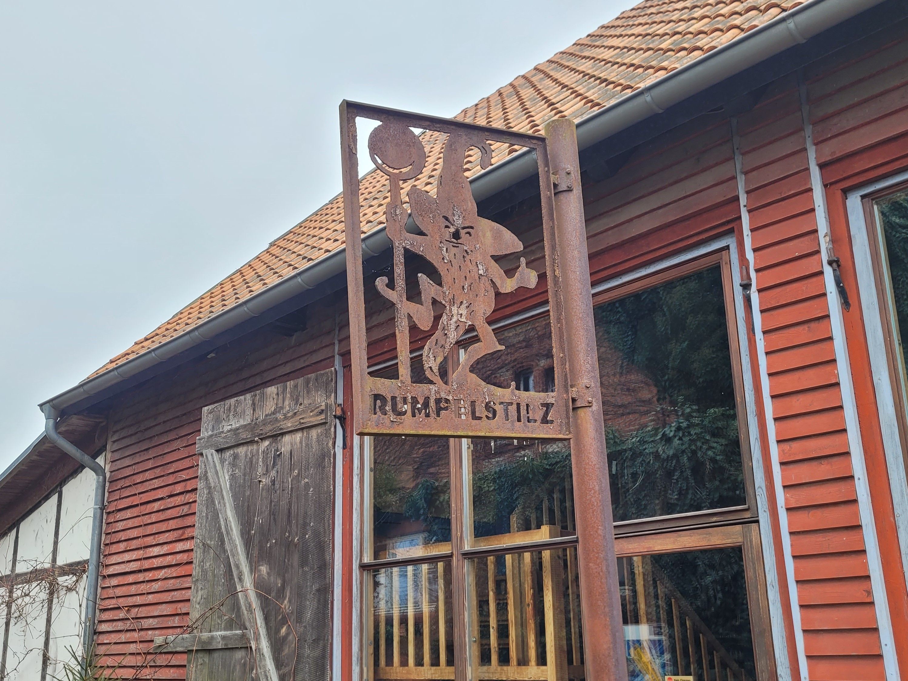 Ein rustikales Gebäude mit einem verwitterten Metallschild mit der Aufschrift "RUMPFSTILZ" und einem traditionellen roten Ziegeldach.