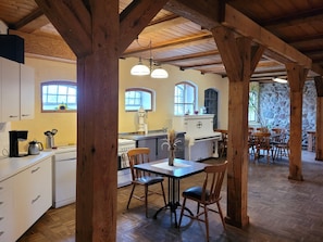 A rustic kitchen with wooden beams, a dining area with wooden chairs, and a stone wall. - Holiday room 1 - RUMPELSTILZ baking and shower barn (Steinhagen)