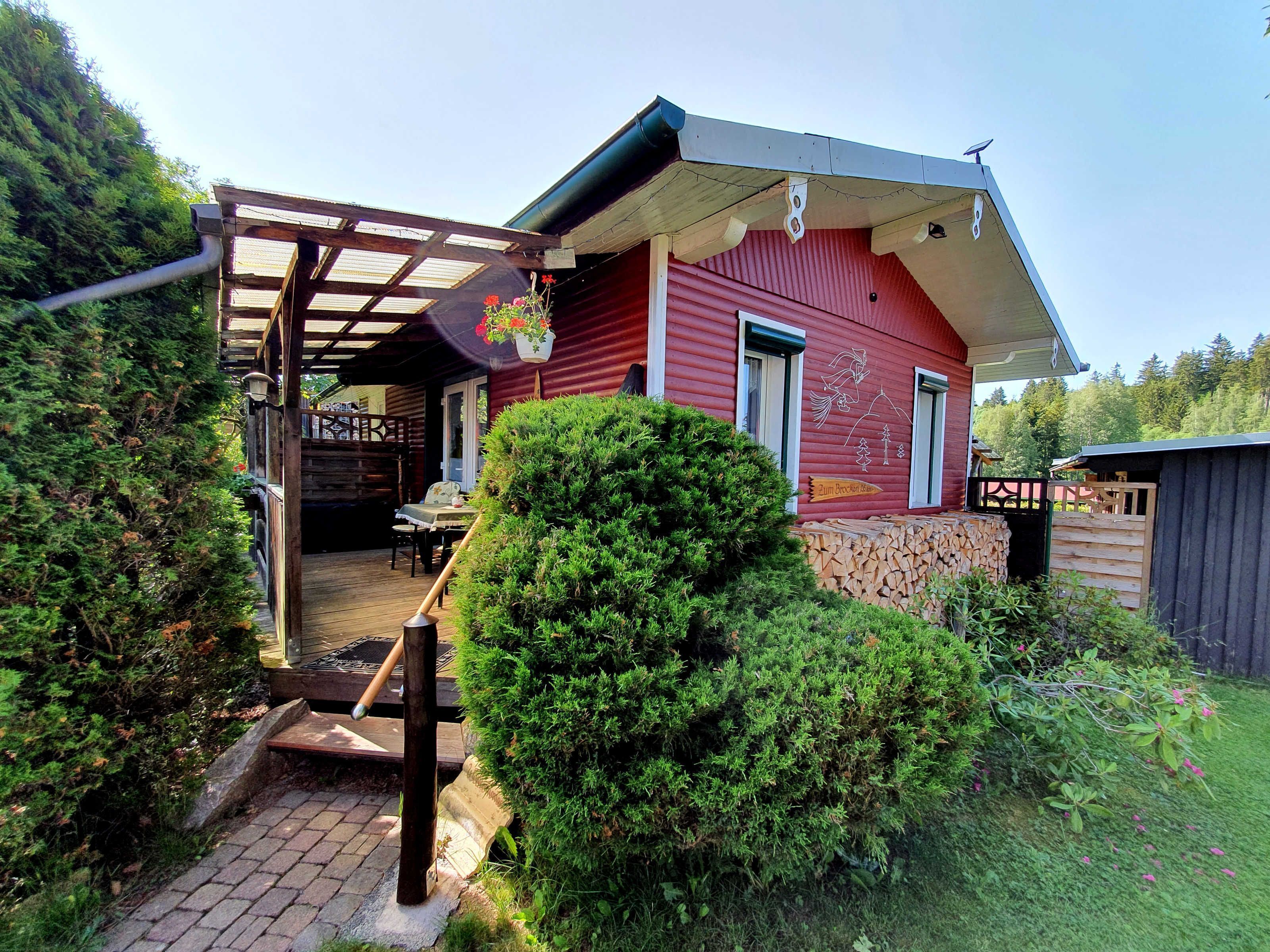 Eine rote Holzhütte mit überdachter Veranda, einer Steinmauer und einem kleinen Garten.