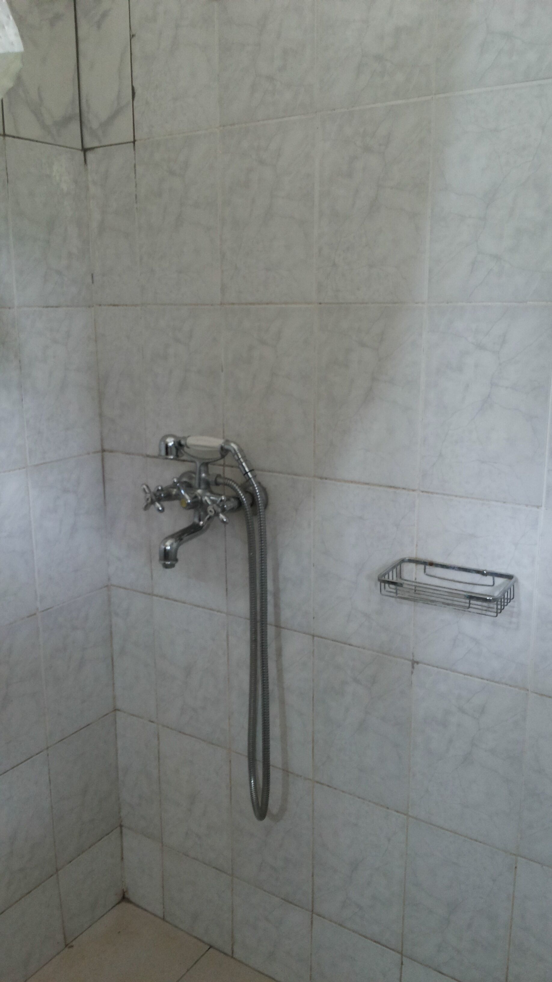 Un baño con ducha, paredes de azulejos y estante metálico.