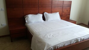 Een slaapkamer met een houten hoofdeinde, een groot bed met witte beddengoed en een nachtkastje.