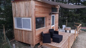A wooden cabin with two large windows, a small door, and a deck with wicker furniture. - peggy's tiny (Sisteron)