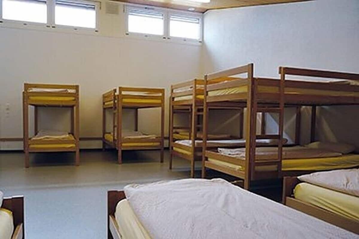 Un dormitorio con literas alineadas, una ventana y una pared blanca lisa.
