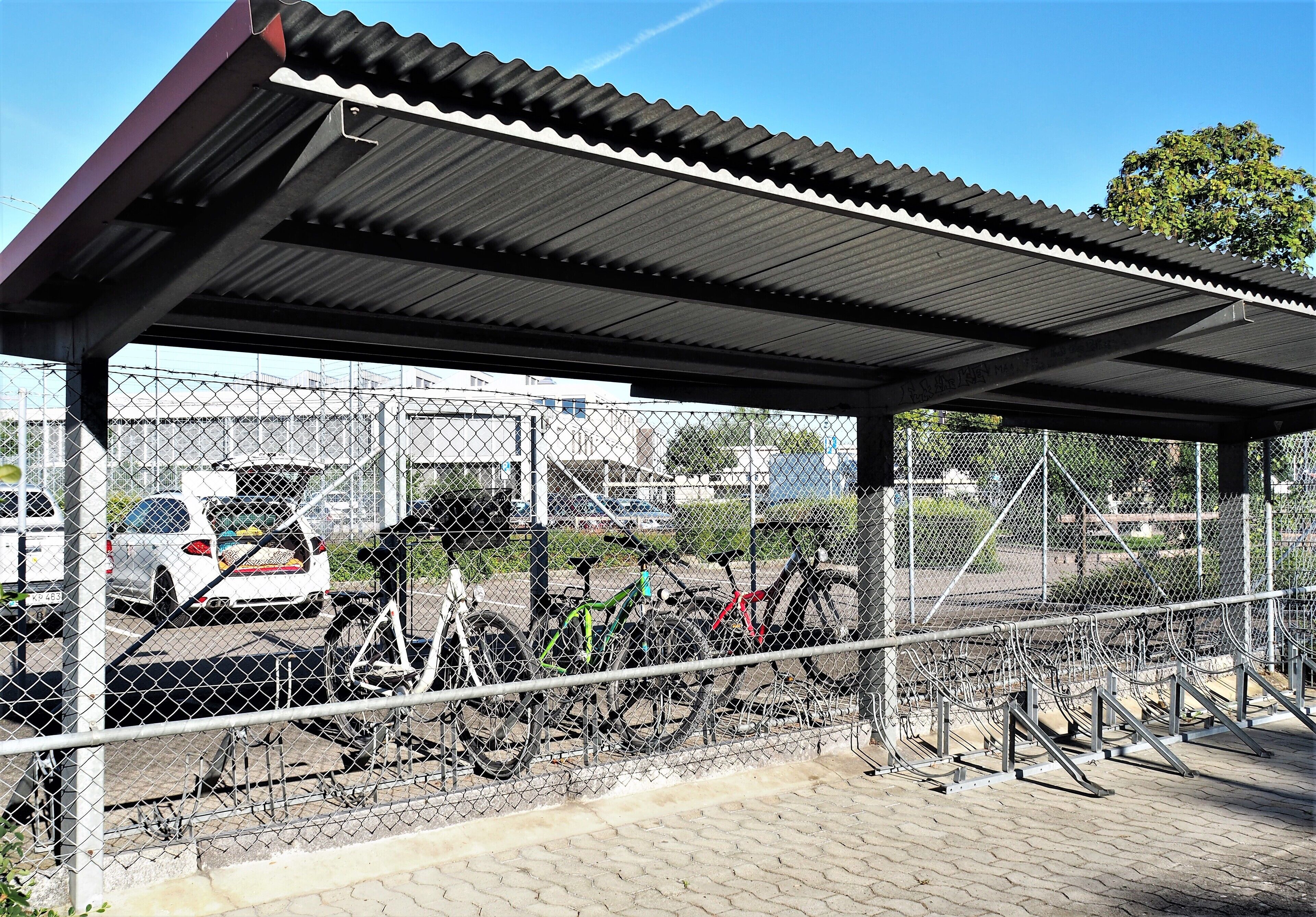Un área de estacionamiento para bicicletas techada con techo metálico y cerca de malla.