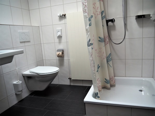 A bathroom with a toilet, a sink, a shower, and a toilet paper holder. - Jugendherberge Romanshorn - Hostel (Romanshorn)