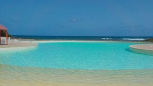 A clear blue pool with a sandy beach and a structure on the left.