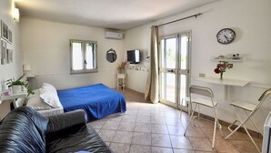 Ett hotellrum med en säng, ett skrivbord, en stol, en tv och en väckarklocka på väggen.