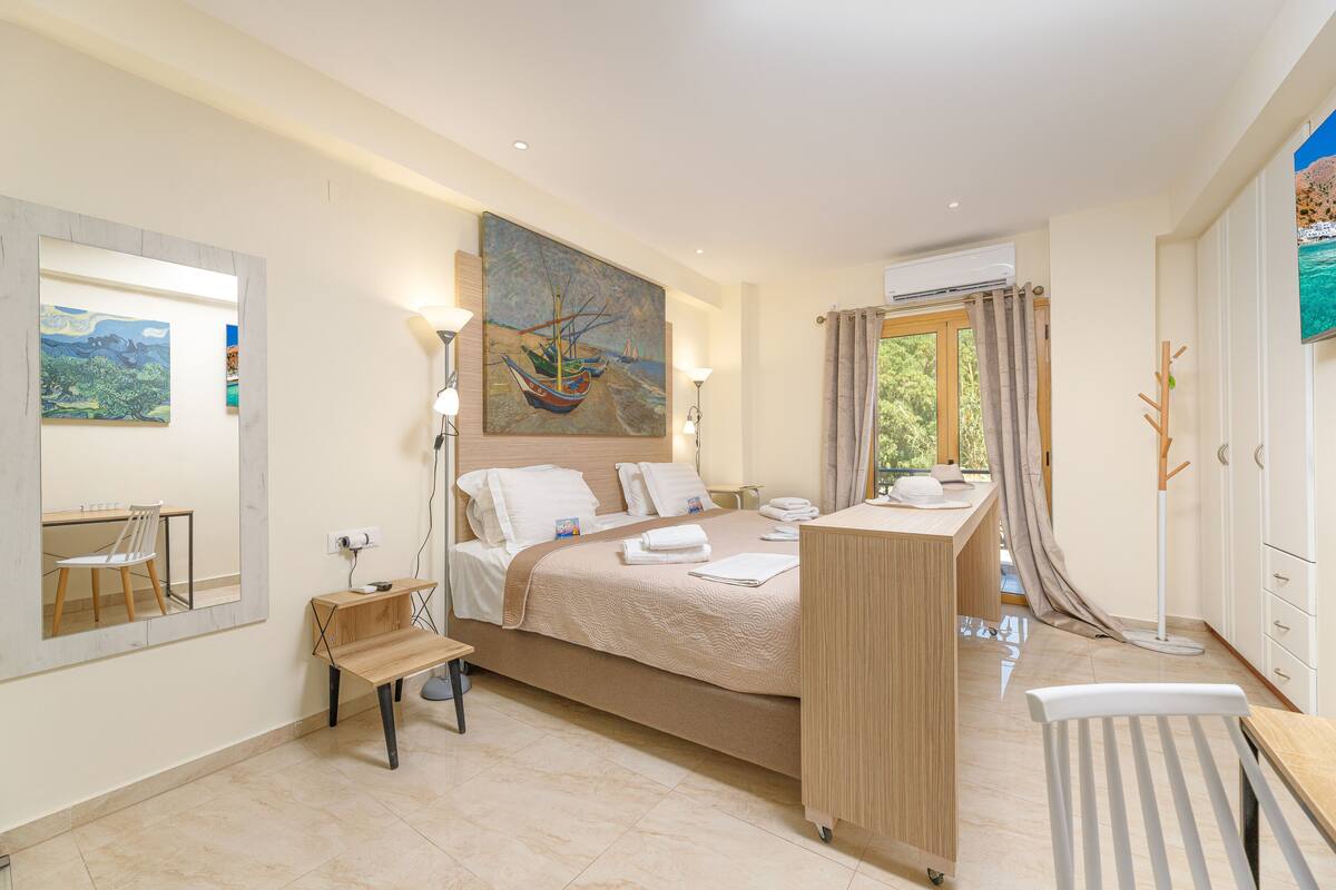 A modern hotel room with a large bed, a desk, a chair, and a painting on the wall.