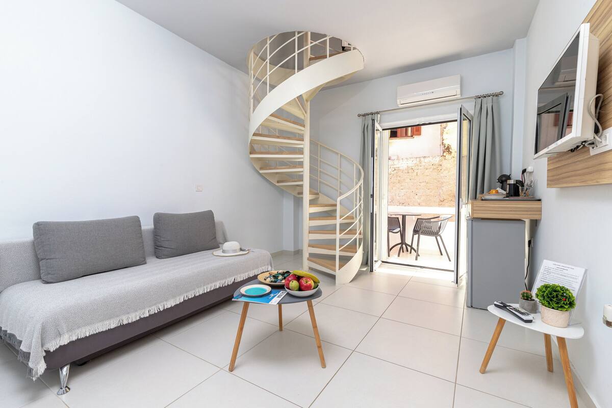 A modern living room with a spiral staircase, a sofa, a small table with fruits, and a TV on a stand.