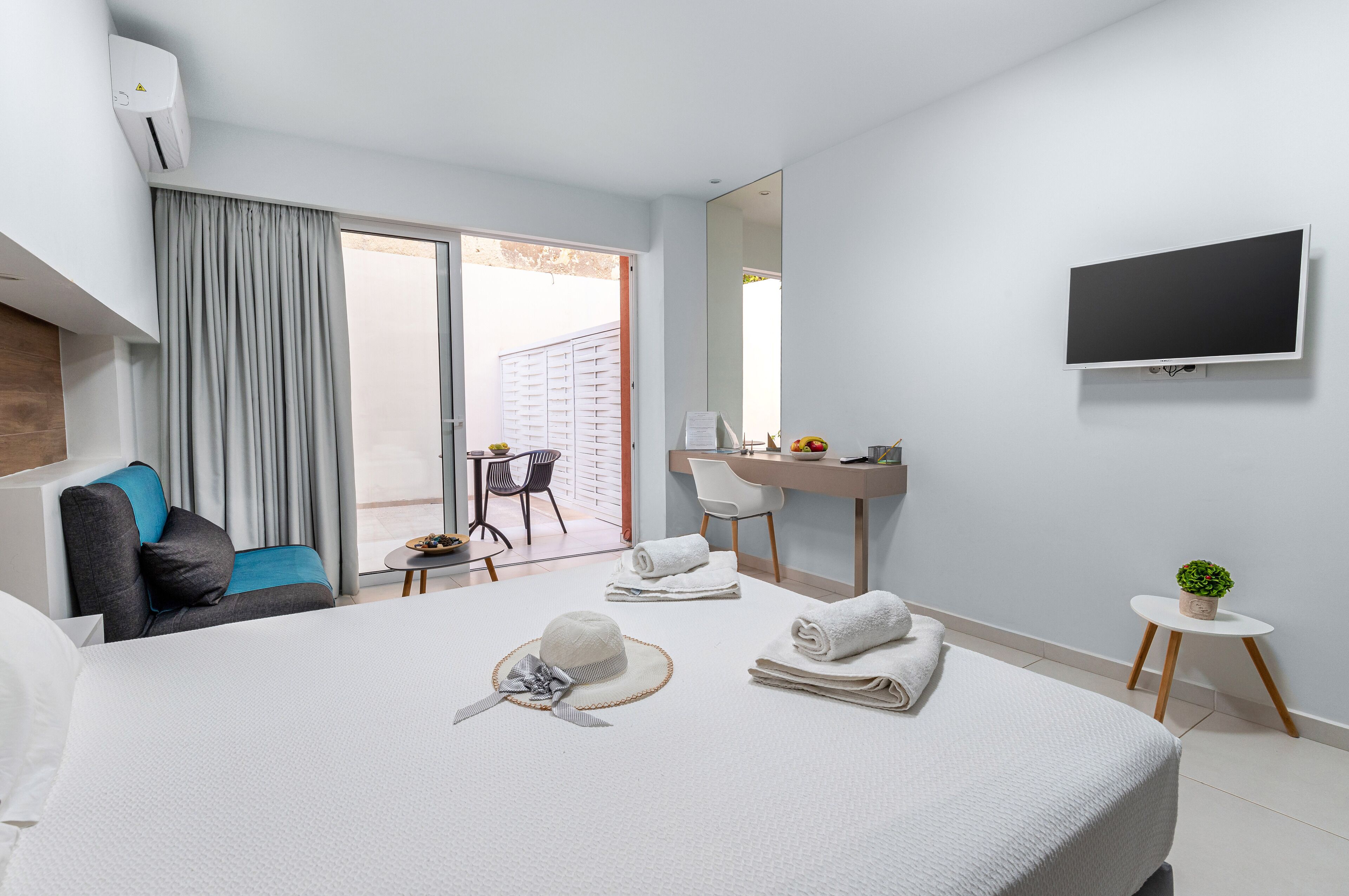 Habitación de hotel con cama, escritorio, televisión, una silla y una pequeña mesa con una planta.