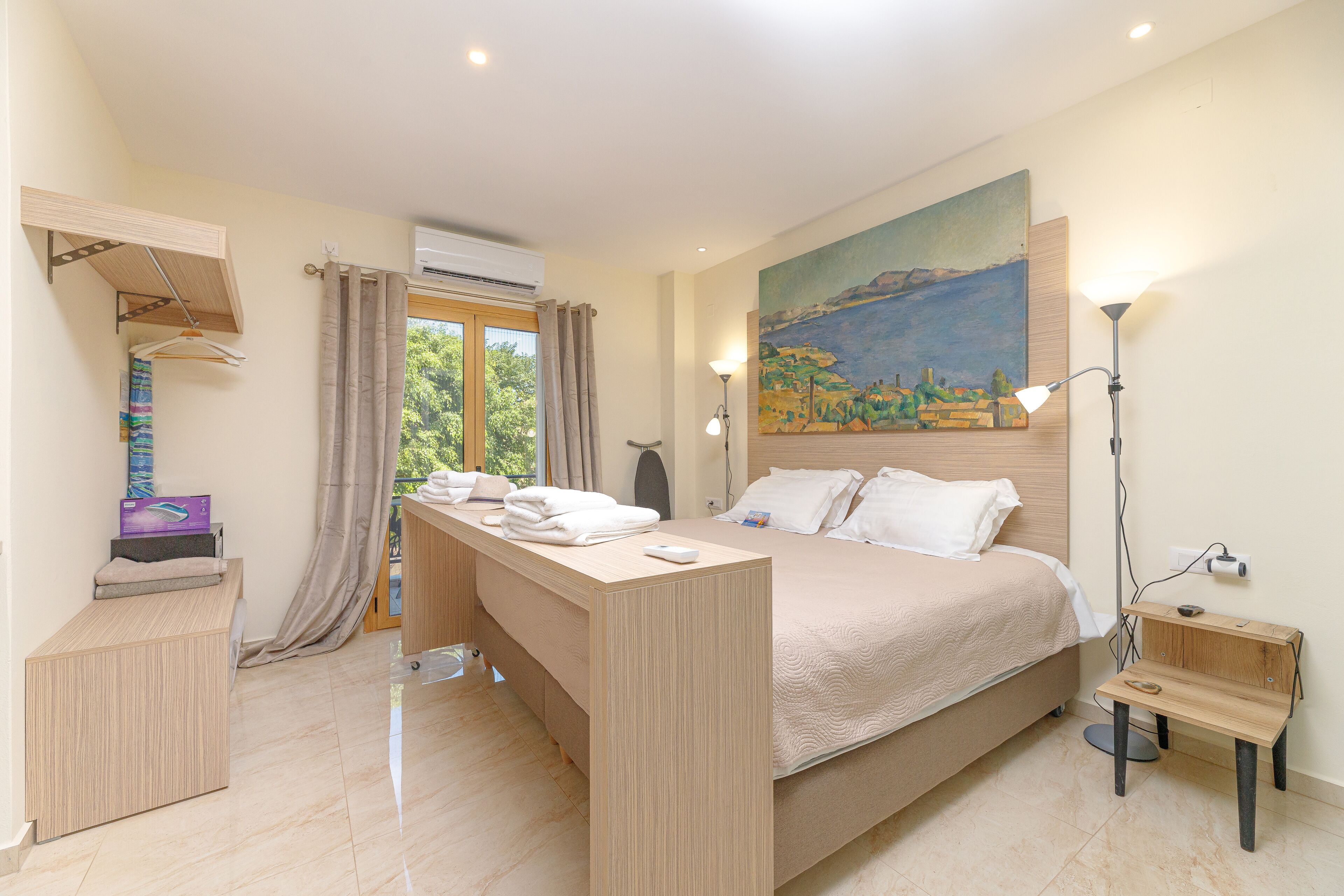 Un dormitorio con cama, mesitas de noche, un escritorio, un cuadro y una ventana con cortinas.