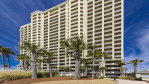 A multi-story hotel with balconies, palm trees, and a clear blue sky.