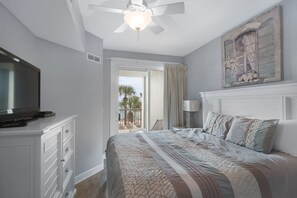 Un dormitorio con cama, televisor sobre un mueble, ventilador de techo y vistas al exterior.