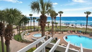 A pool area with palm trees, lounge chairs, and a view of the beach and ocean.