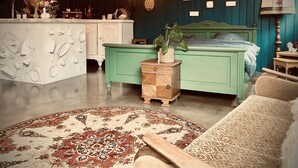 A room with a green bed, a white dresser, a small wooden nightstand, and a patterned rug.
