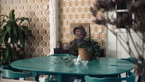 A round table with teal chairs, a vase with a plant, and a painting on the wall.