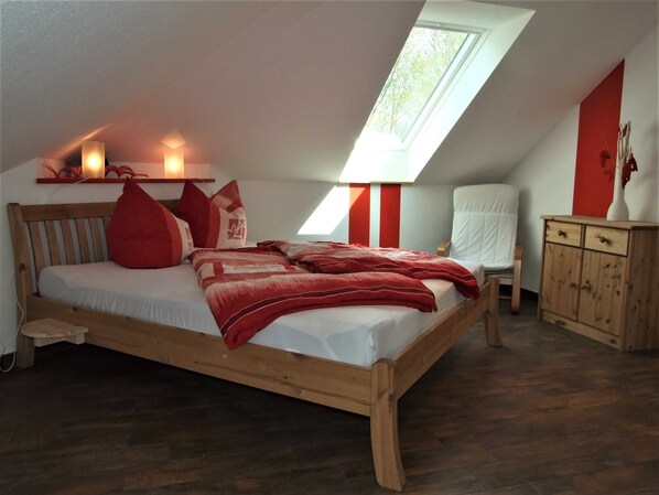 A bedroom with a sloped ceiling, a skylight, a wooden bed, a bedside table, a chair, and a cabinet. - Kranichzug Vacation Apartment - Property ID 120077 (Kargow)