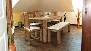 Un comedor con mesa y sillas de madera, un banco, una lámpara colgante y un florero con plantas.