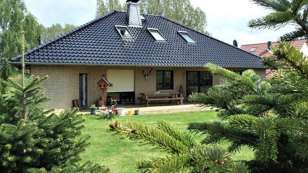 Una casa con techo inclinado, tragaluces, fachada de ladrillo y un césped cuidado con pinos.