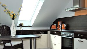 Una cocina moderna con tragaluz, piso de madera oscura, armarios blancos y un comedor con una silla de mimbre y un jarrón de flores.