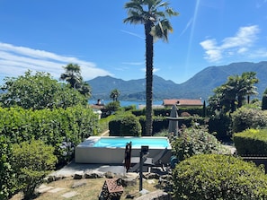 A pool area with lounge chairs, surrounded by lush greenery and a mountain backdrop. - La nostra casa - Welcome to Ghiffa on Lake Maggiore (Ghiffa)