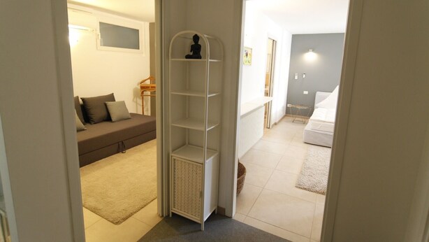 A hallway leading to a bedroom with a bed, a white wardrobe, and a small shelf with a statue.